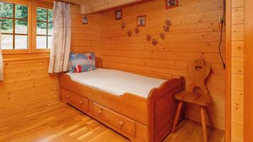 Une pièce de cabane en bois comprenant un lit, une chaise et une fenêtre avec des rideaux.