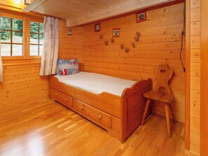 Ein Zimmer in einer Holzhütte mit einem Bett, einem Sessel und einem Fenster mit Vorhängen.