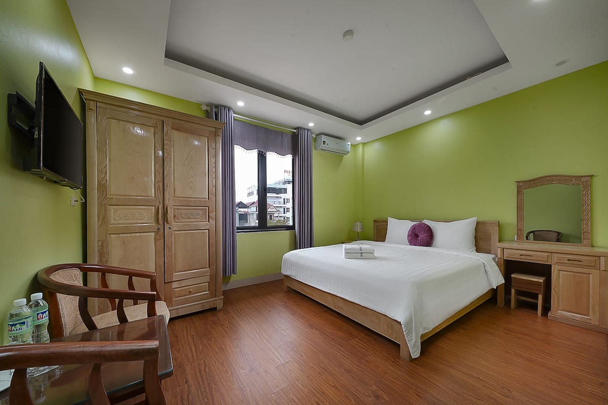 A hotel room with a bed, wooden wardrobe, desk, chair, and a television.