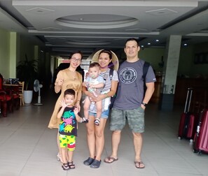 A family of four in a hotel lobby with a modern ceiling design, a seating area with chairs and tables, and a fan on the floor. - Golden Lotus Airport Hotel  (Hanoi)