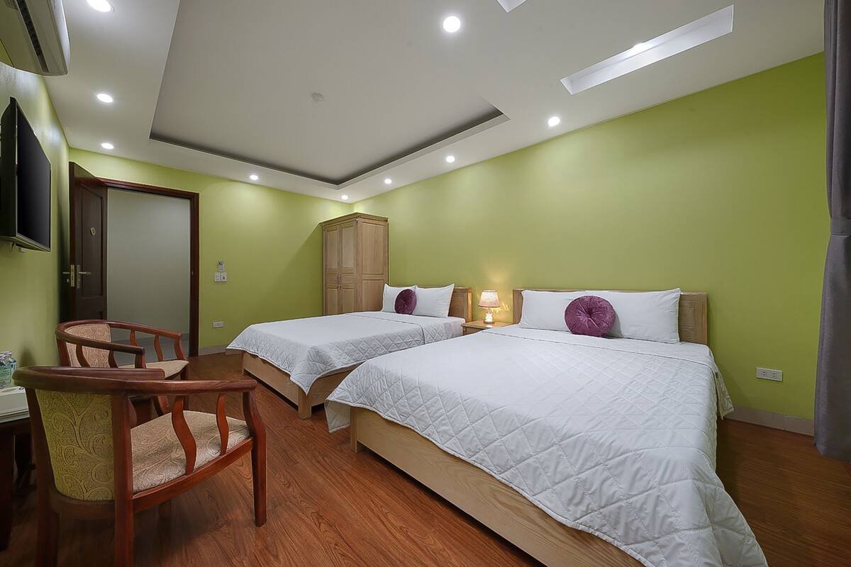 A hotel room with two beds, a wooden wardrobe, a desk with a chair, and a television.