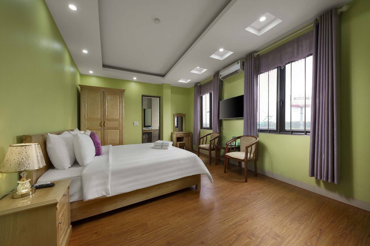 A hotel room with a bed, bedside table, lamp, and a TV on the wall.