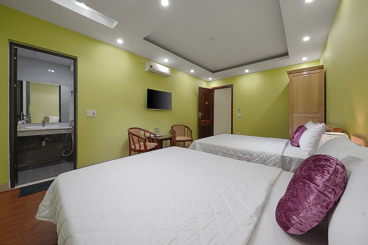 A hotel room with two beds, a television, a desk with chairs, and a bathroom with a mirror and sink.