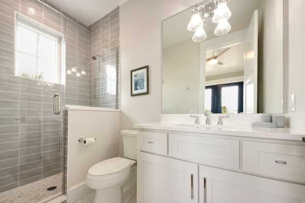 Une salle de bain moderne avec une douche à parois de verre, des toilettes, un lavabo avec un miroir et un ventilateur de plafond.