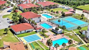 An aerial view of a resort with multiple swimming pools, a tennis court, and a large covered area.