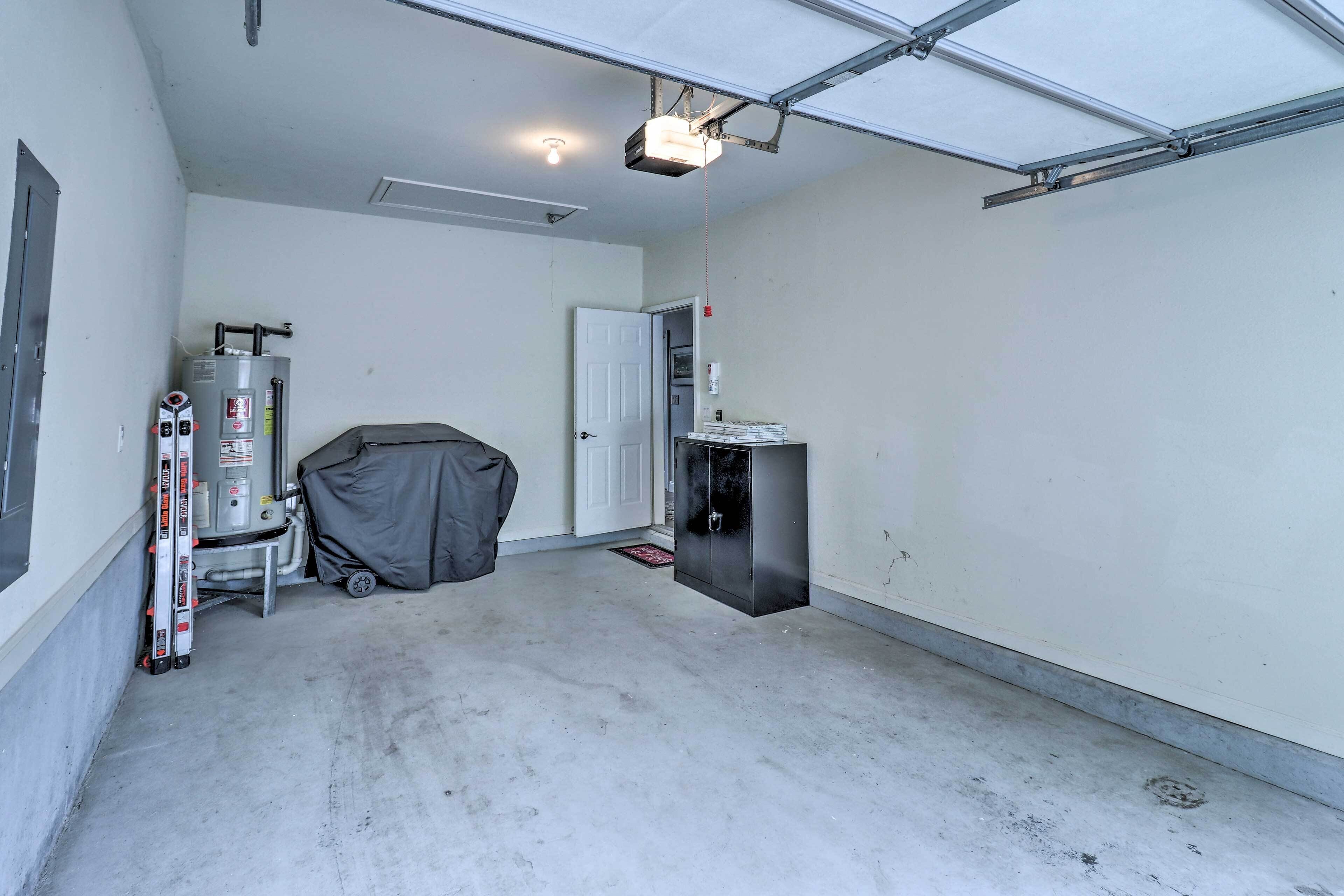 A garage with a water heater, a covered grill, and a cabinet.
