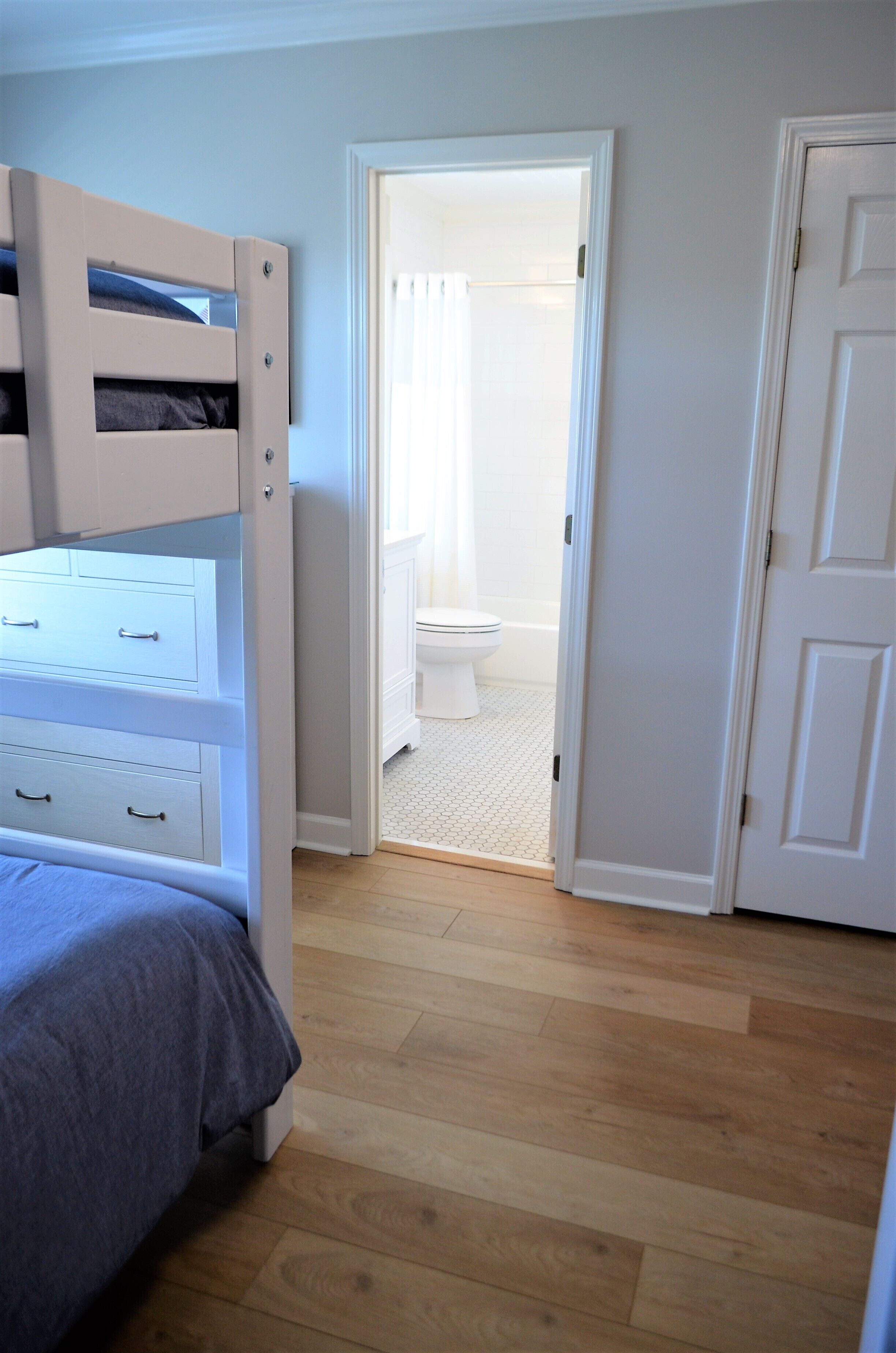 A bedroom with a bunk bed, a door leading to a bathroom, and a wooden floor.