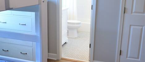 A bedroom with a bunk bed, a door leading to a bathroom, and a wooden floor.