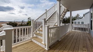 Een houten terras met een witte balustrade en een trap naar een overdekt gedeelte.