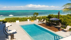 A pool area with lounge chairs and umbrellas, overlooking a turquoise sea. - Villa DelEvan 4C / 1-bedroom villa on the Grace Bay Beach, (Providenciales)