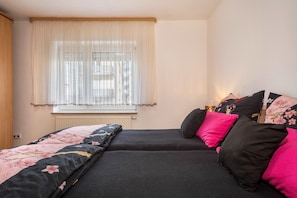 A bedroom with a bed, a window with sheer curtains, and a wall-mounted radiator.