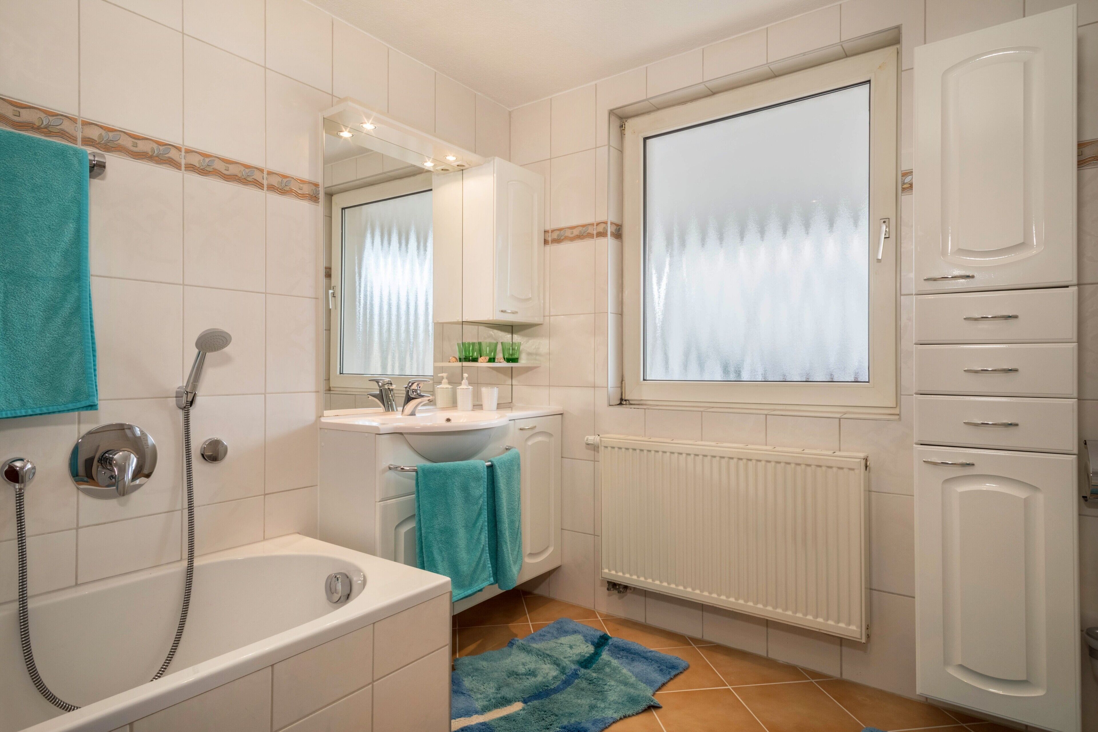 Ein Badezimmer mit einer Badewanne, einem Waschbecken, einem Spiegel, einem Fenster und einer Heizung.