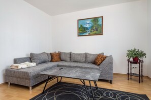 A living room with a grey sectional sofa, a small table, a painting of a landscape, and a potted plant.