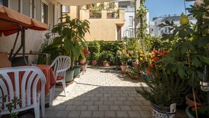 A patio with potted plants, a table with a red tablecloth, and white chairs. - Apartment 'Grüne Oase' with Shared Terrace, Shared Garden and Wi-Fi (Friedrichshafen)