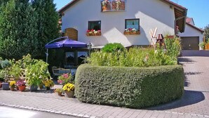 Ein zweistöckiges Gebäude mit Balkon, Topfpflanzen und einem gepflasterten Einfahrt.