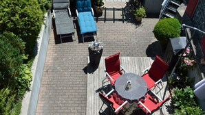 Eine Terrasse mit einem runden Tisch, roten Stühlen, einem blauen Sofa und einer Mülltonne.