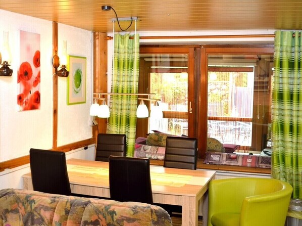 A dining area with a wooden table, chairs, and a view through a glass door.