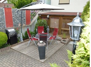 A patio with a grill, red chairs, a table, and a lantern.