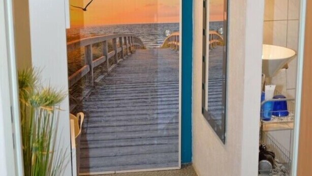 Ein Flur mit Blick auf einen hölzernen Steg, der zu einem Sonnenuntergang über dem Wasser führt.