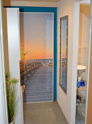 A hallway with a view of a wooden pier leading to a sunset over the water.