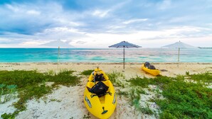 Una playa con dos kayaks amarillos y una sombrilla.