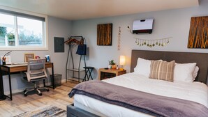 A hotel room with a large bed, a desk with a chair, a small table with a lamp, and a window with a view. - Bellevue Guesthouse by Lake Sammamish, Patio (Bellevue)