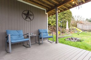 Un área de estar al aire libre con techo, con dos sillas azules acolchadas y una mesita, una decoración de estrella en la pared y una terraza de madera.