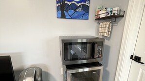 A compact kitchenette with a microwave and oven, a coffee machine, a painting on the wall, and a small shelf with toiletries. - Bellevue Guesthouse by Lake Sammamish, Patio (Bellevue)