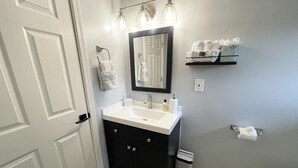 A bathroom with a white sink, dark cabinet, and a mirror above it. There are towels and toiletries on the wall. - Bellevue Guesthouse by Lake Sammamish, Patio (Bellevue)
