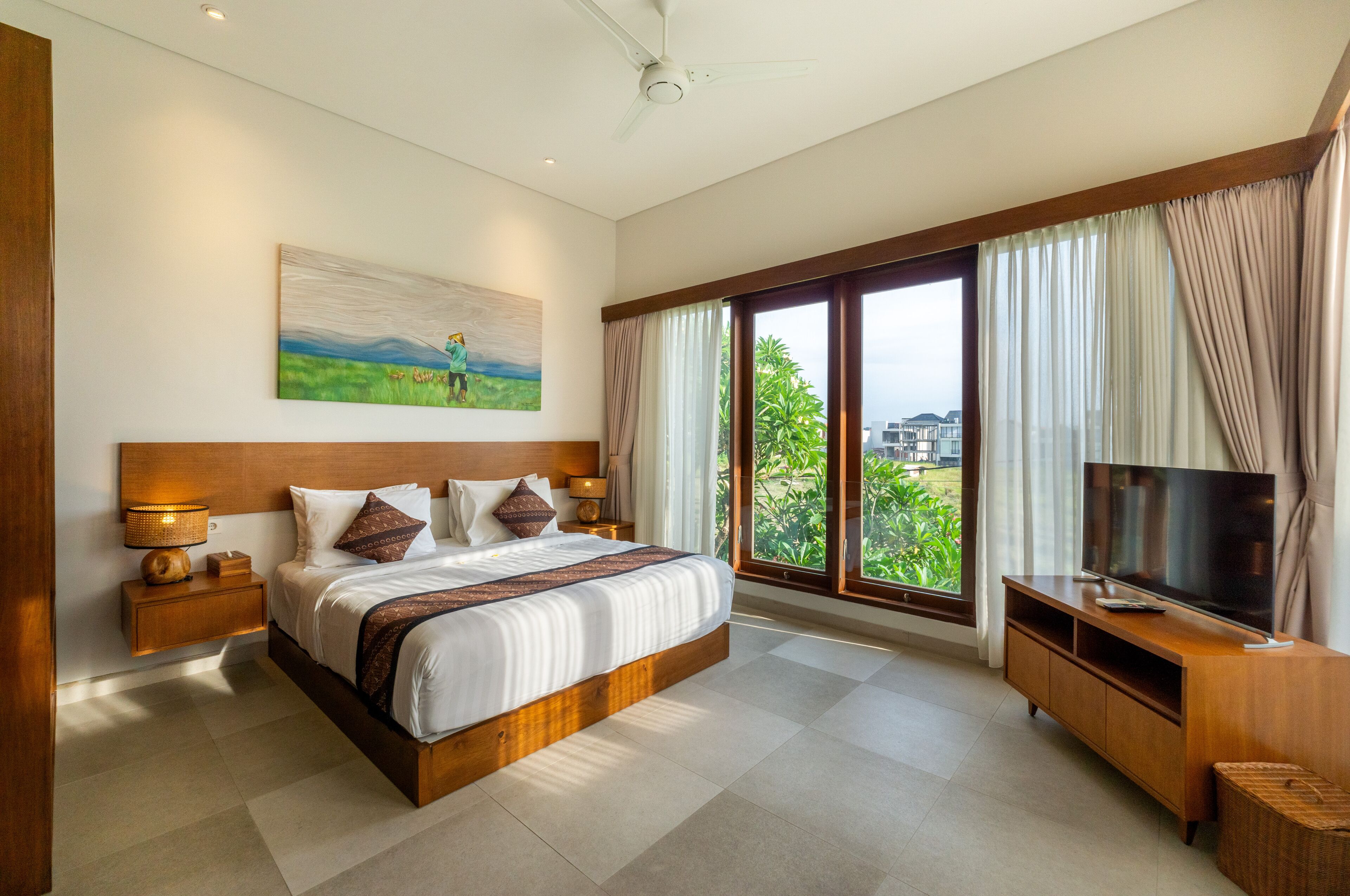 A spacious bedroom with a large bed, a TV, and a view of greenery outside.