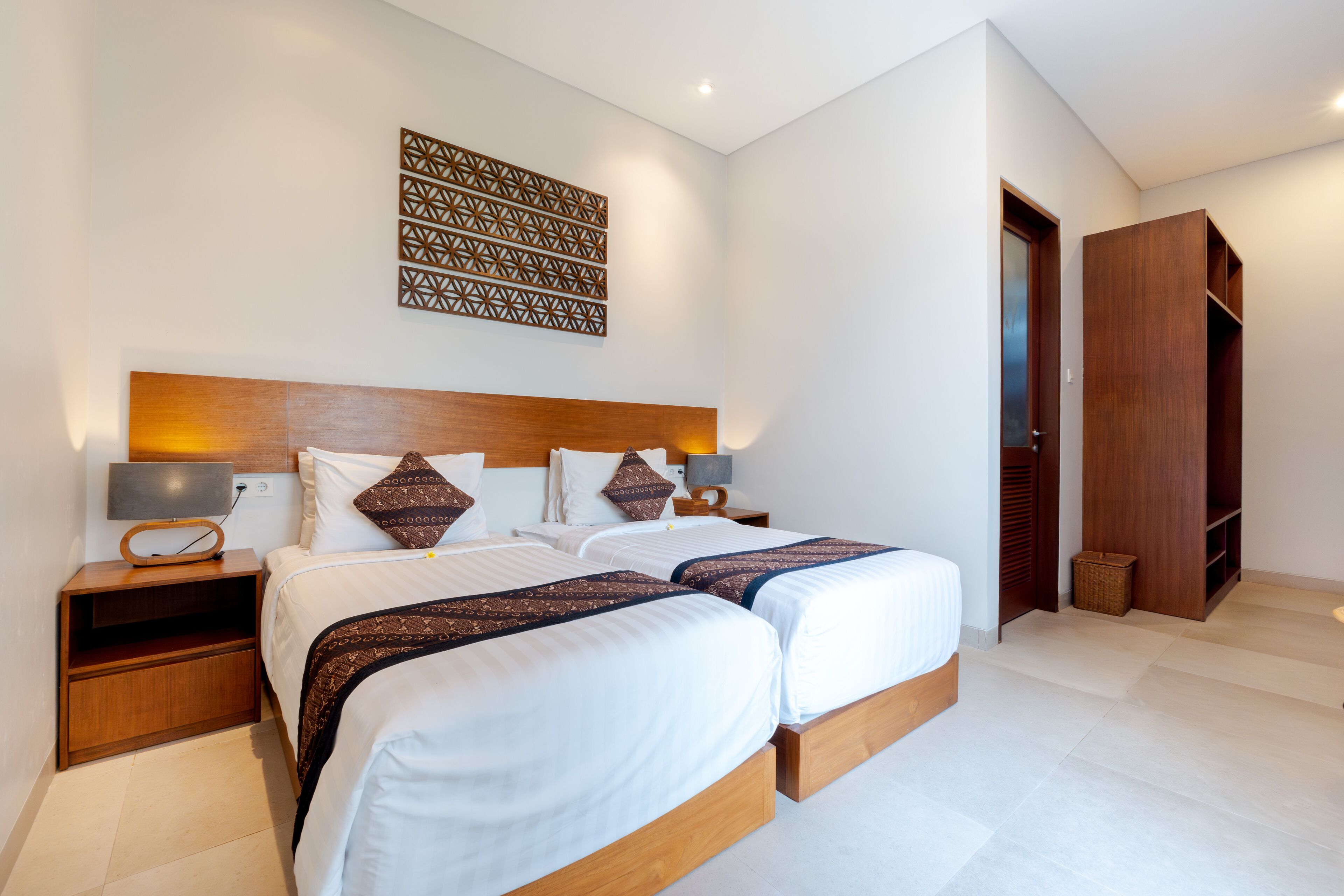A modern hotel room with two beds, a wooden headboard, a decorative wall panel, and a wardrobe.