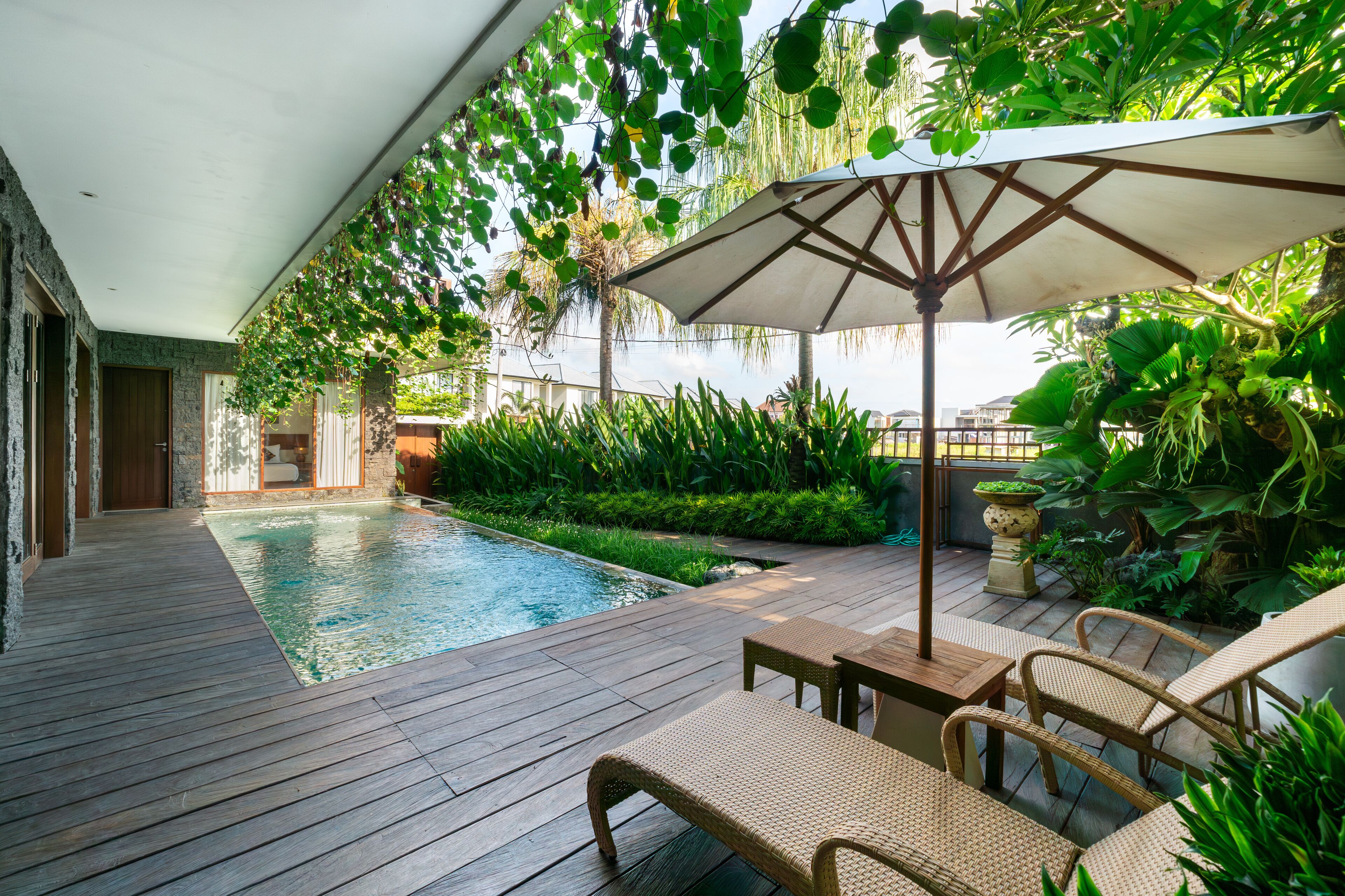A wooden deck with a pool, wicker furniture, and lush greenery.