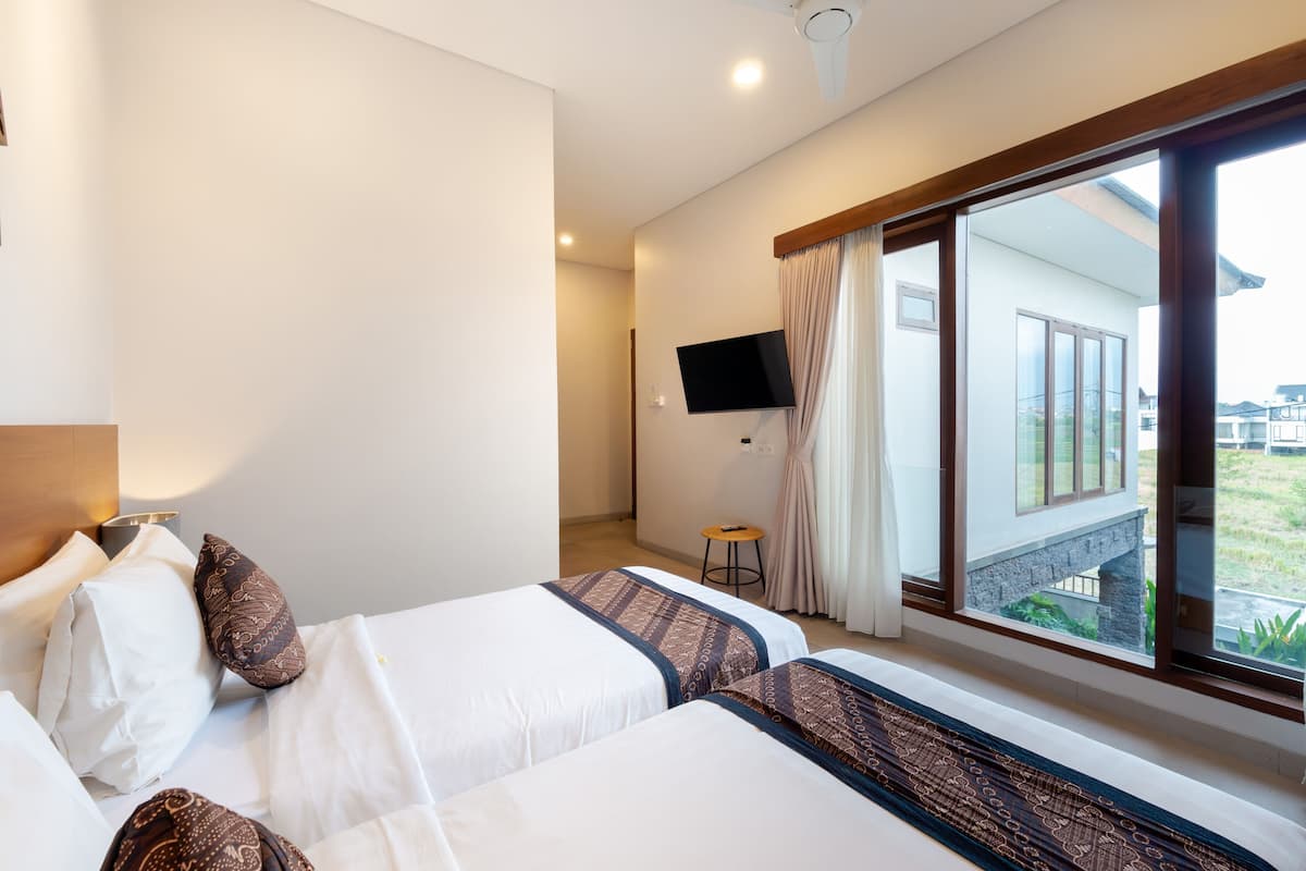 A hotel room with two beds, a TV mounted on the wall, and a large window with a view of the outside.