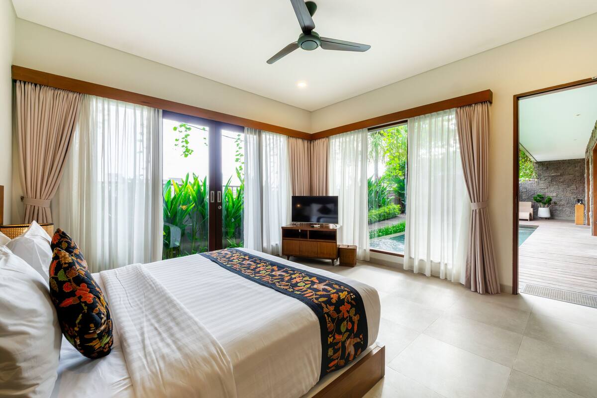 A spacious bedroom with a large bed, a ceiling fan, and a TV.