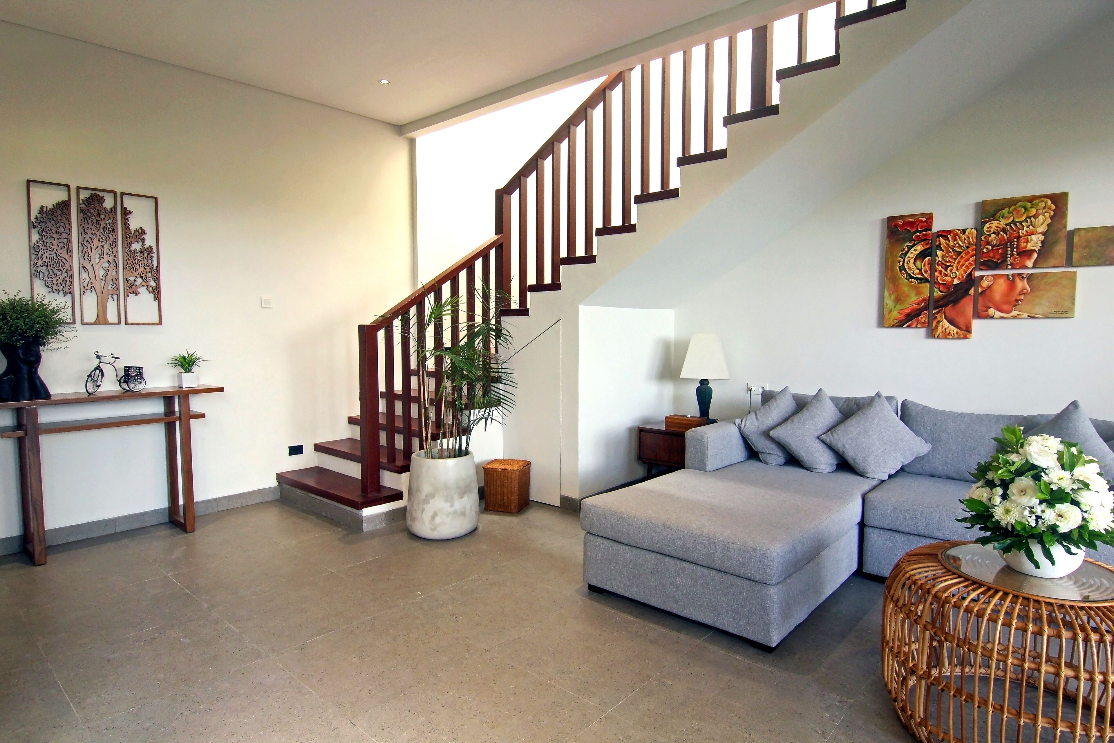 A modern living room with a grey sofa, a wooden staircase, and artwork on the walls.