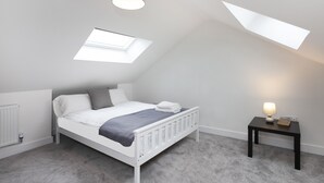 Ein Schlafzimmer mit Bett, Nachttisch mit Lampe, Heizkörper und Dachfenster.