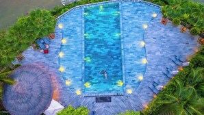 An aerial view of a rectangular swimming pool with a surrounding deck, surrounded by lush greenery and palm trees. - Hoi An Memories Resort & Spa (Da Nang)
