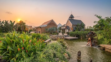 A traditional building with a water wheel, surrounded by lush greenery and a pond.