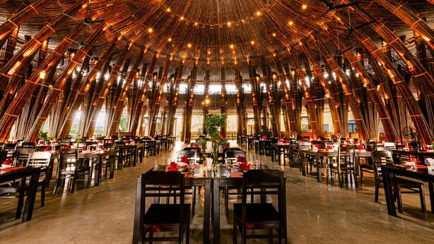 A spacious dining area with high ceilings and bamboo structures, featuring multiple tables and chairs arranged for dining. - Hoi An Memories Resort & Spa (Da Nang)