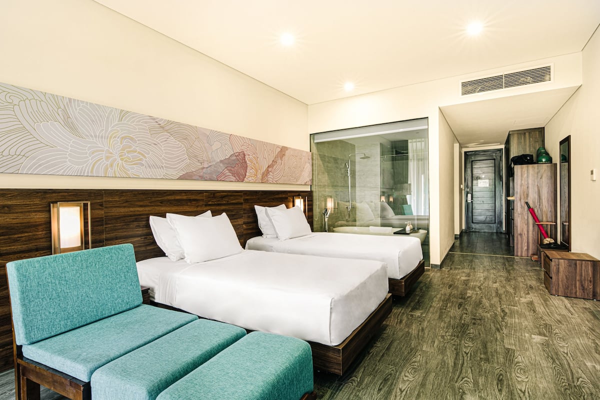 A hotel room with two beds, a seating area, a shower, and a hallway leading to a bathroom.