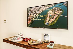 A television displaying a welcome sign for Hoi An Memories Resort & Spa, with a wooden table in front featuring traditional conical hats, a plate of food, and a QR code.