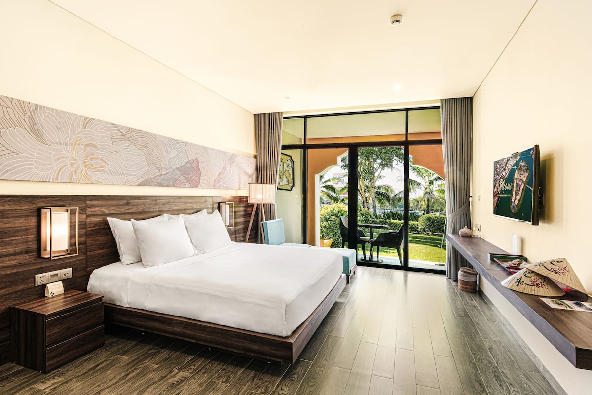 A modern hotel room with a large bed, wooden headboard, and a view of the outdoors.