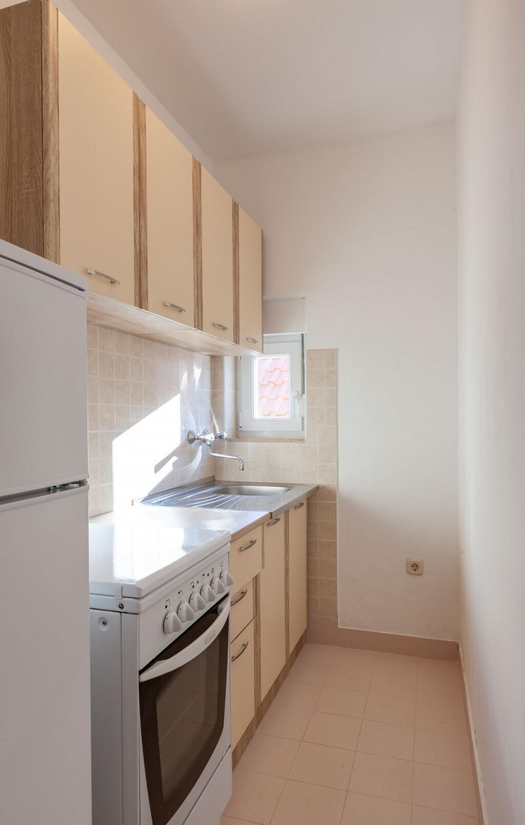 A compact kitchen with a stove, oven, and sink. There is a window with a view of the outside.