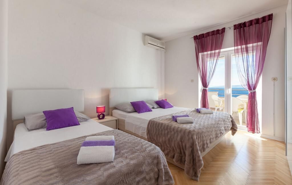 A hotel room with two beds, a nightstand, a lamp, and a view of the sea through large windows.