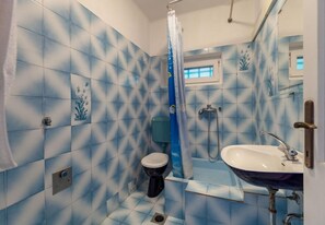A bathroom with blue patterned tiles, a white toilet, a shower with a blue curtain, and a white sink with a mirror above it. - Apartments Nena (Omis)