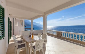 Un espace extérieur abrité, doté d’une table et de chaises, offrant une vue sur la mer, ainsi qu’un balcon avec une balustrade.