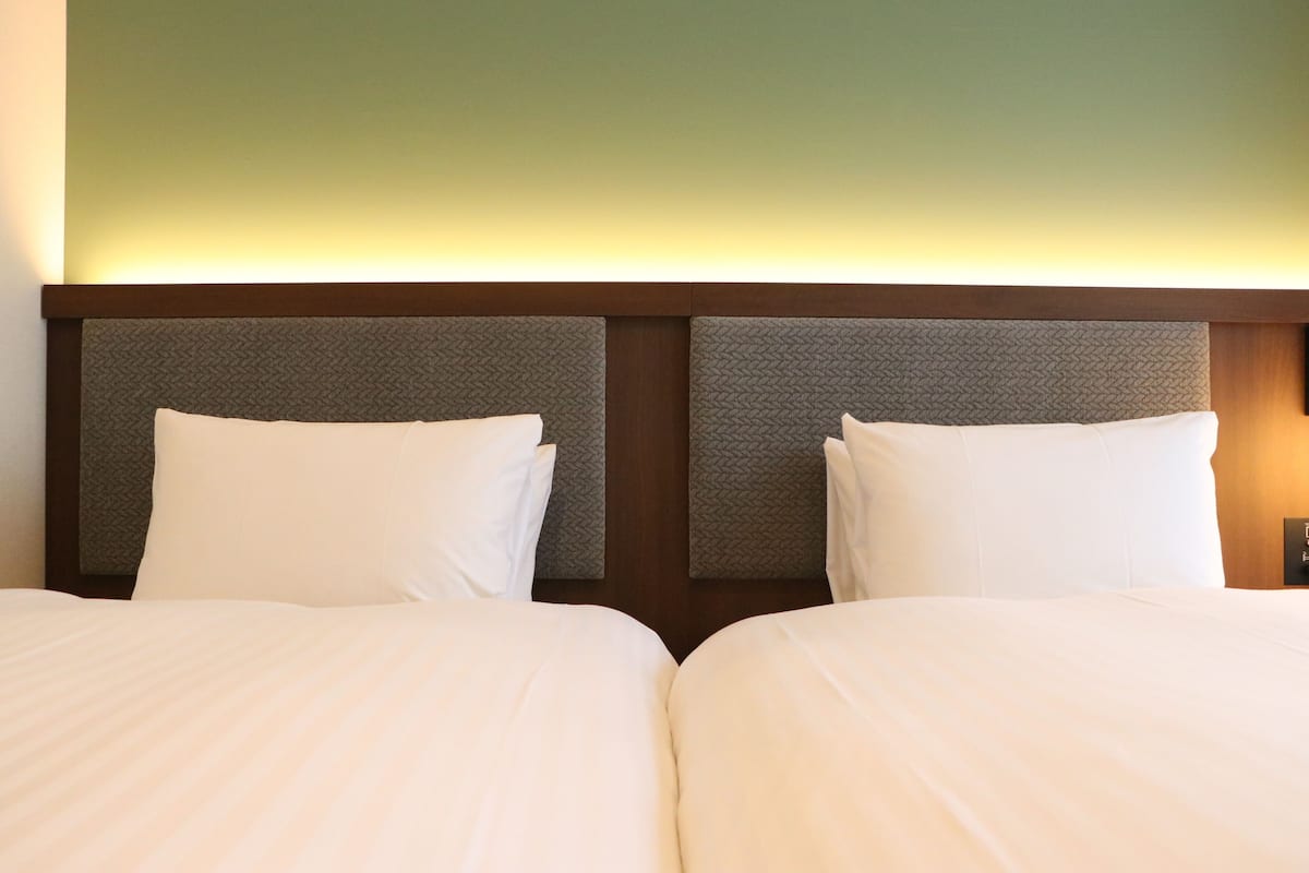 Hotellihuone, jossa on kaksi sänkyä, puinen pääty ja vihreä seinä.