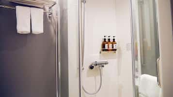 Une douche fermée par des parois en verre, dotée d’un pommeau de douche à main et d’un robinet mural. Deux bouteilles de shampoing et d’après-shampoing sont posées sur une étagère au-dessus de la douche.