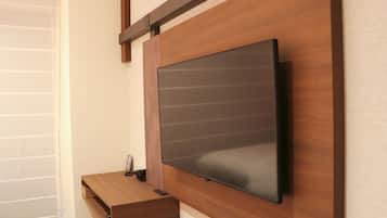 A modern room with a mounted flat-screen TV on a wooden wall, a wooden desk with a drawer, and a window with blinds.