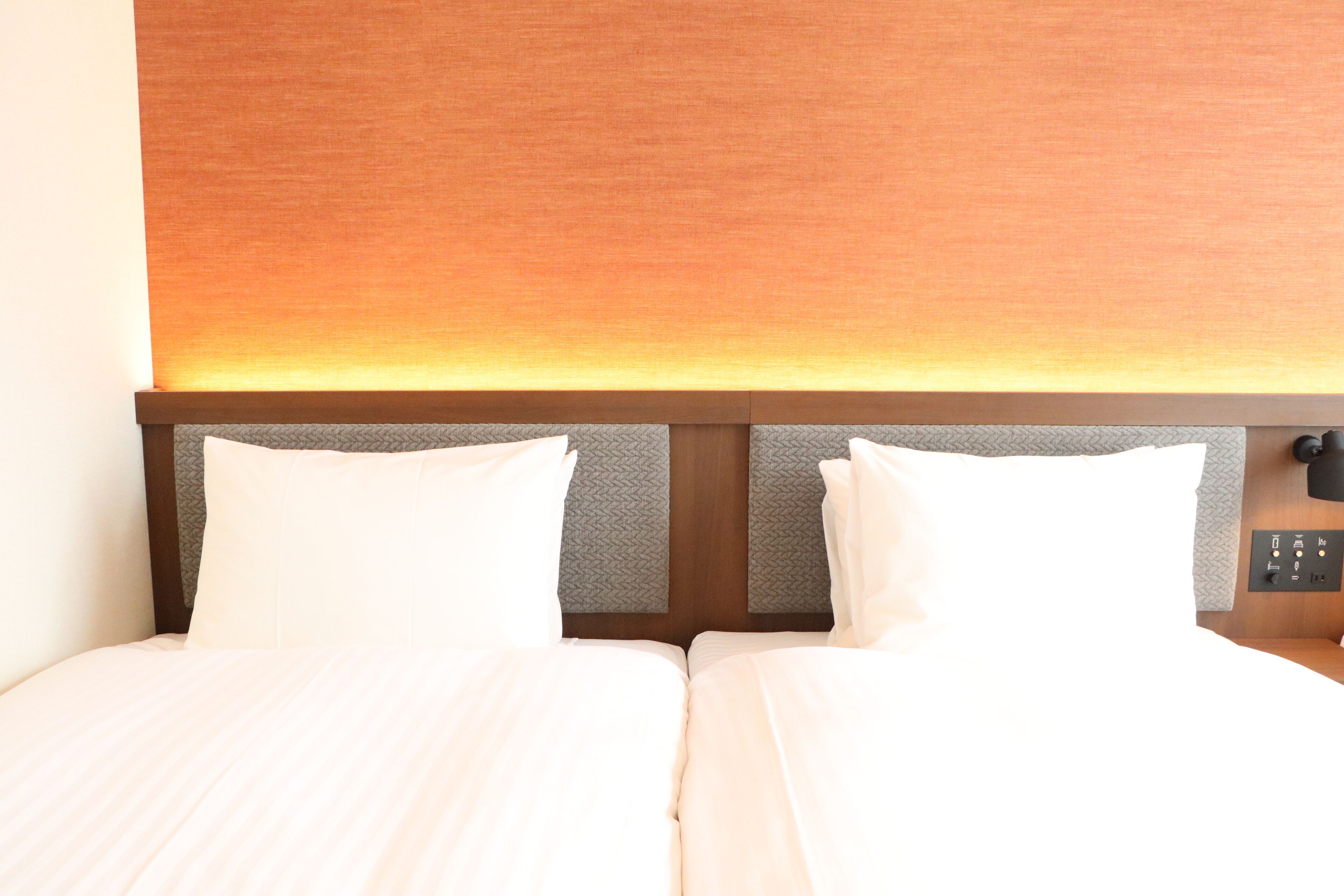 A double bed with white linens, a wooden headboard, and a control panel on the side.